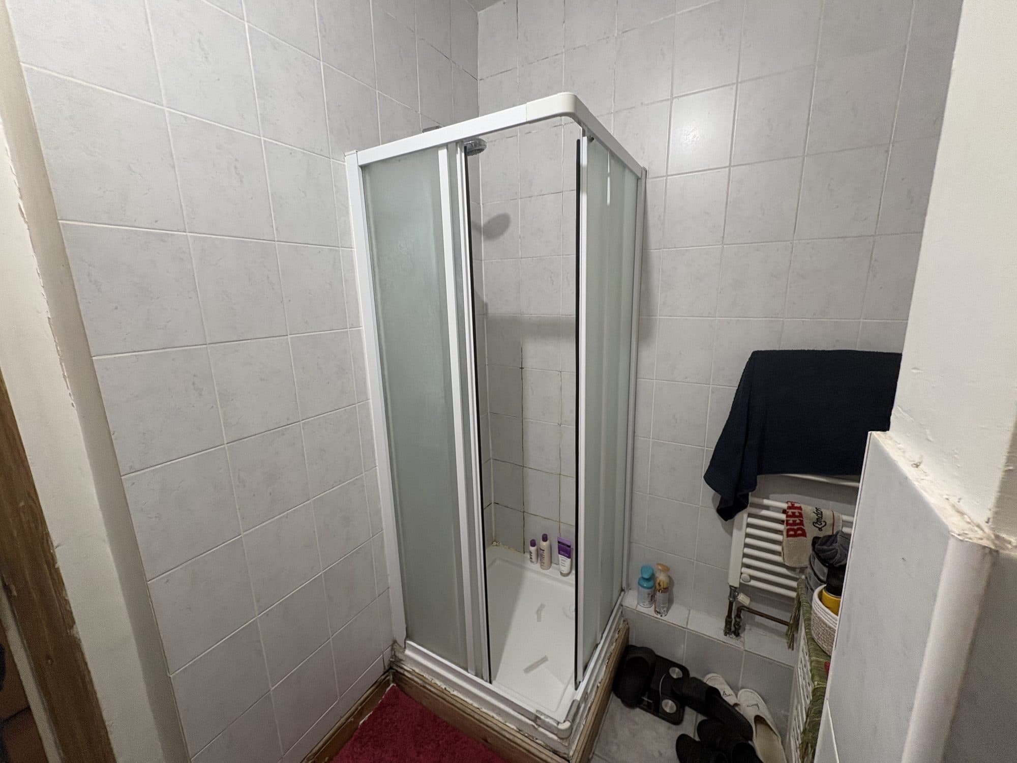 Existing corner shower enclosure with frosted sliding doors in a tiled bathroom, before the work