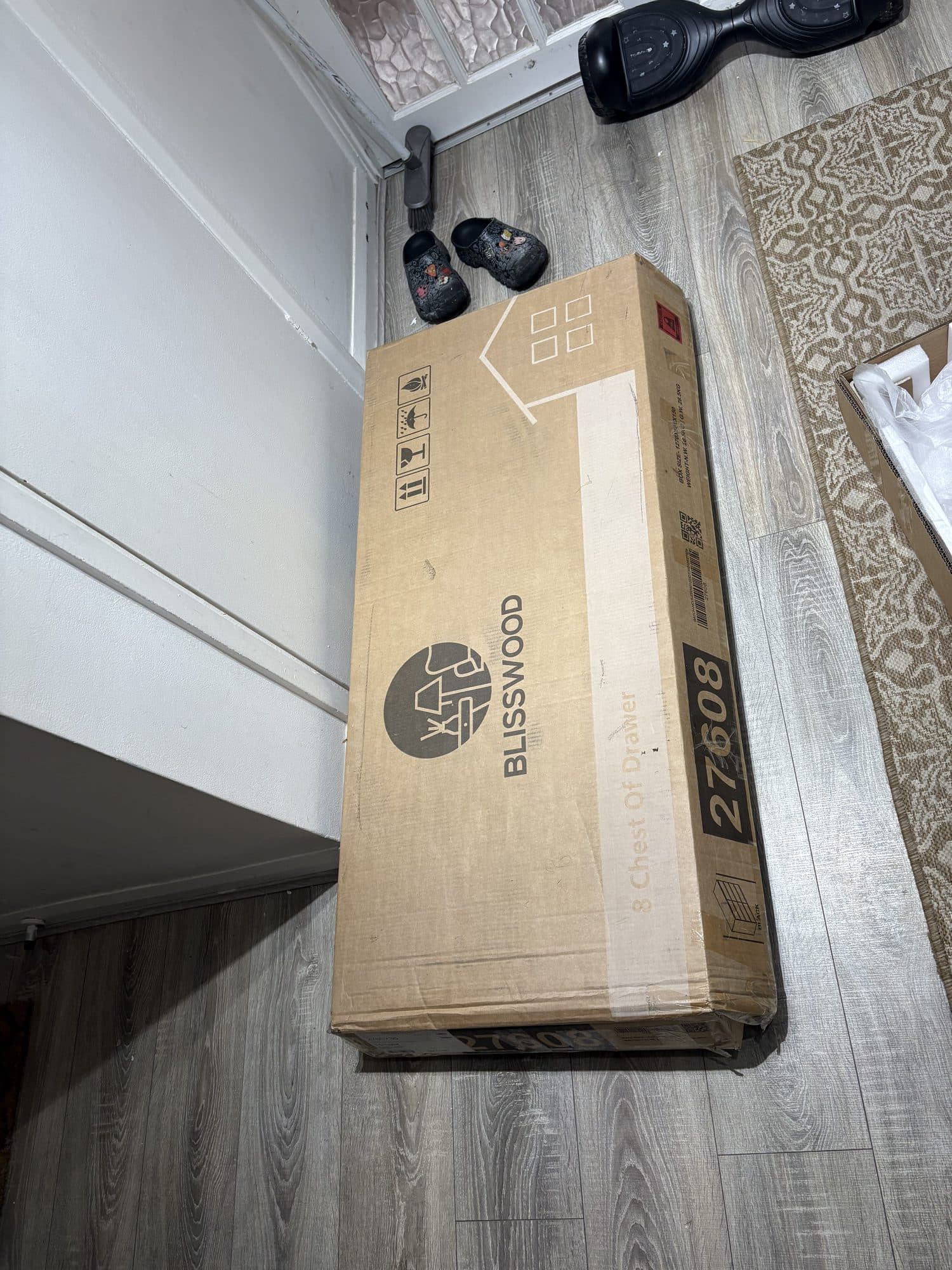 Boxed flat-pack chest of drawers lying on a wood-effect floor before assembly