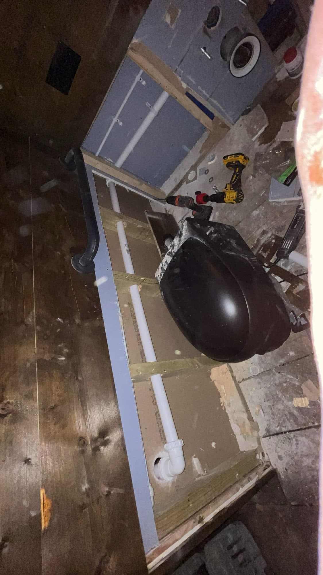 Waste and water pipework and a sink bowl in the restricted space beneath a bar, with a cordless drill alongside, during plumbing work